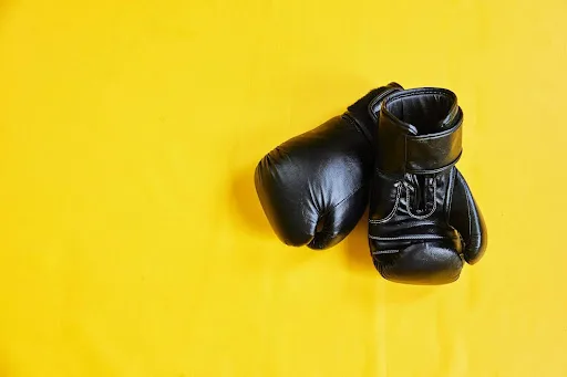 Pair of black boxing gloves on a yellow background.