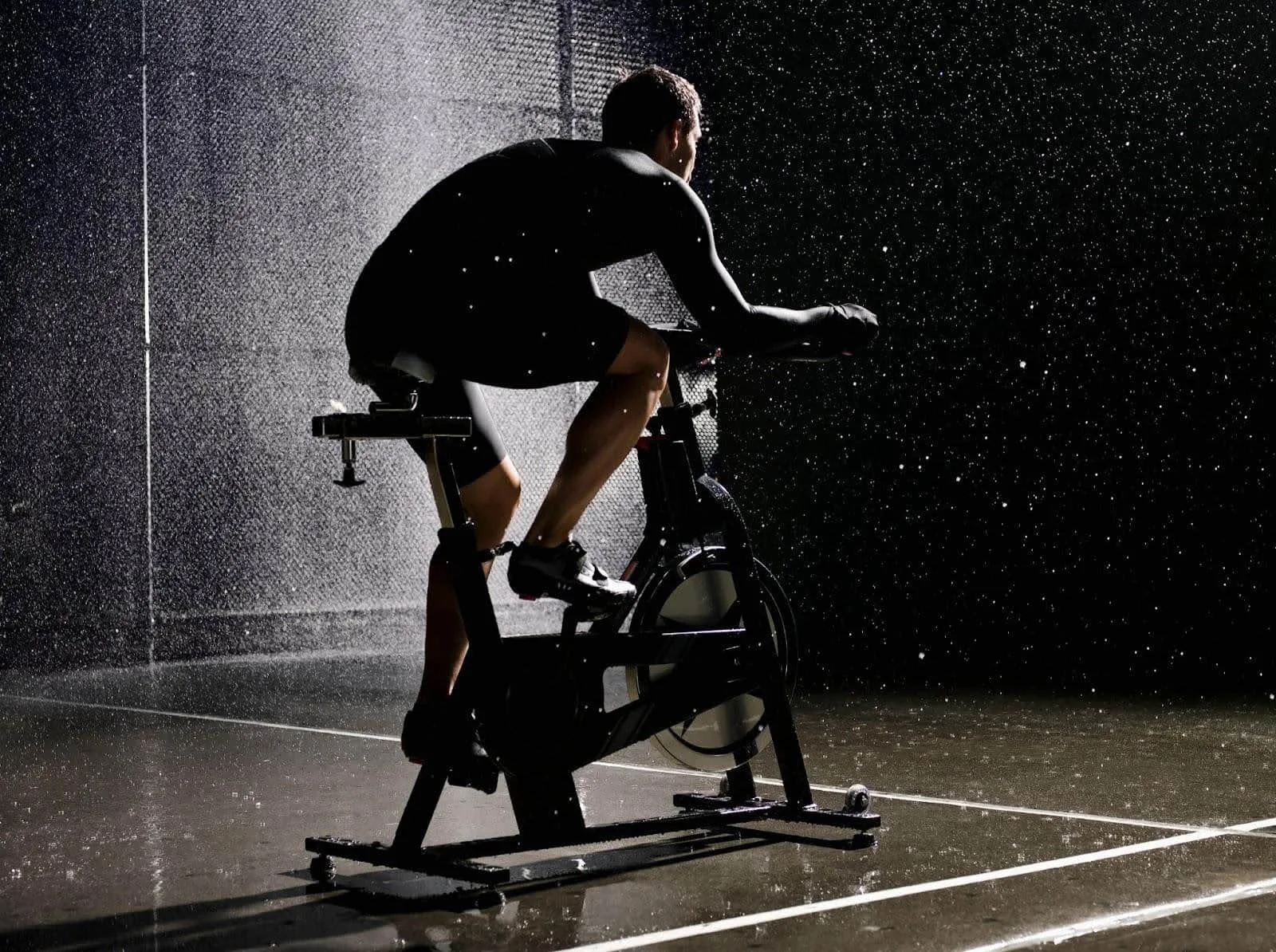 Person cycling indoors on a stationary bike in dim lighting.