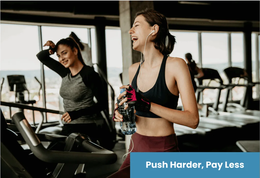 Two women laughing and working out on treadmills in a bright modern gym.